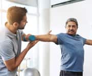 older man lifting a dumbell under the guidance of a personal trainer