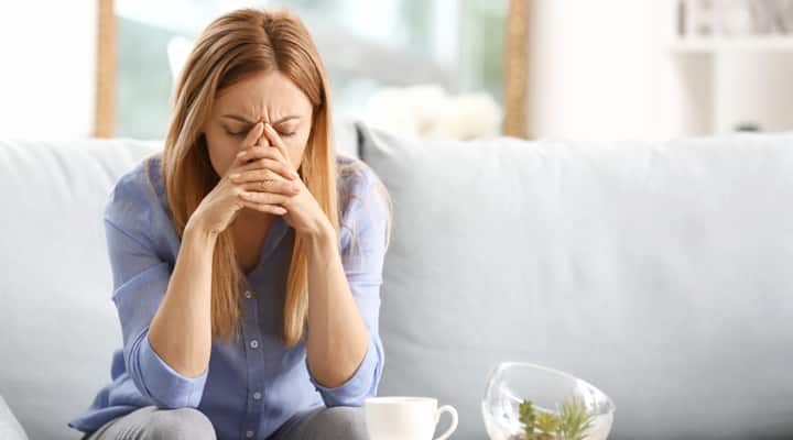Woman sitting on couch feeling fatigue and holding her head