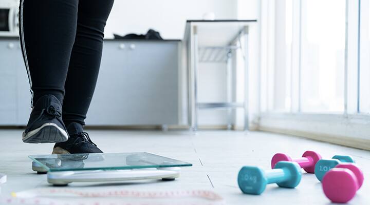Woman stepping on scale for checking weight gain due to sleep loss