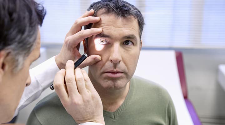 Eye doctor using light to check man's eye for retinopathy