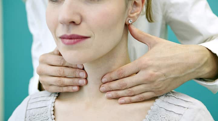 Doctor pressing on woman’s neck to examine her thyroid