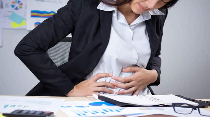 Business woman clutching her abdomen in pain due to gallstones