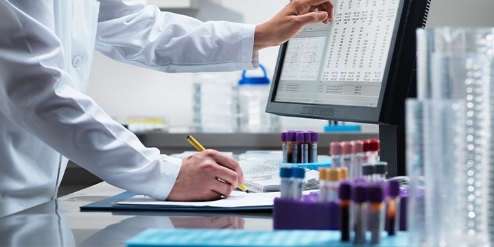 Scientist look at computer next to test tubes and writing something