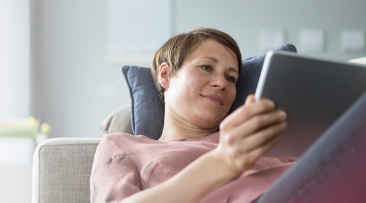 Woman relaxing on a couch reading her tablet