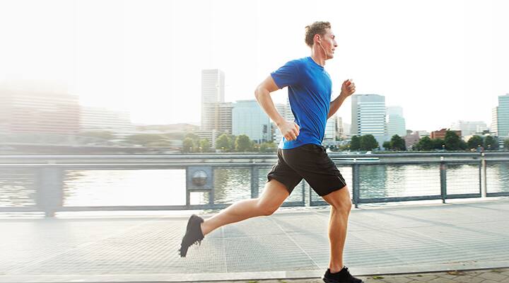 Fit man with earphones jogging along city riverside