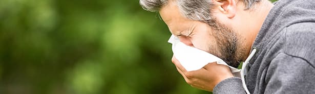 Man sneezing into tissue due to seasonal allergies