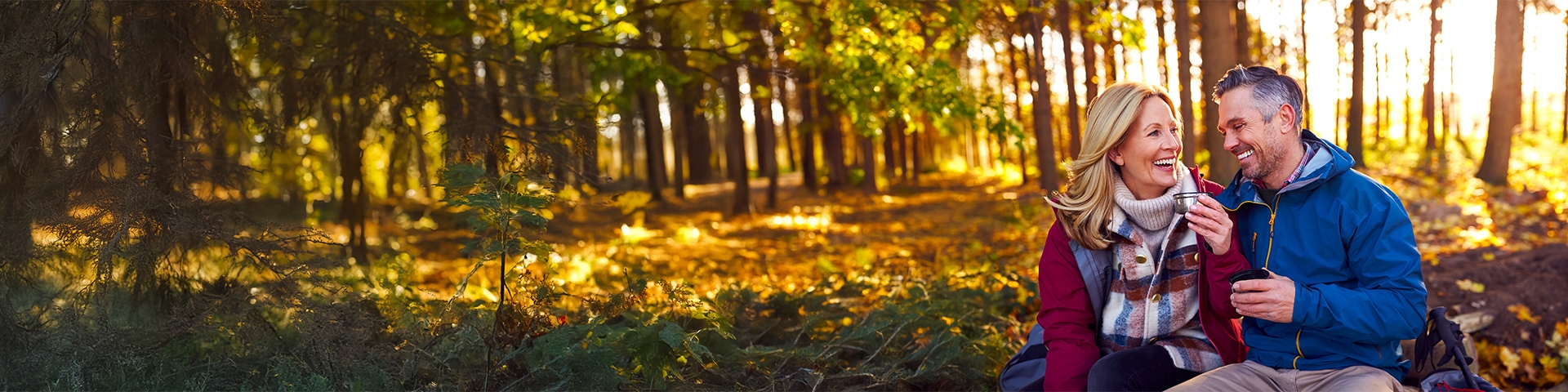 A middle-aged couple savoring hot drinks amidst the golden hues of a peaceful fall forest.