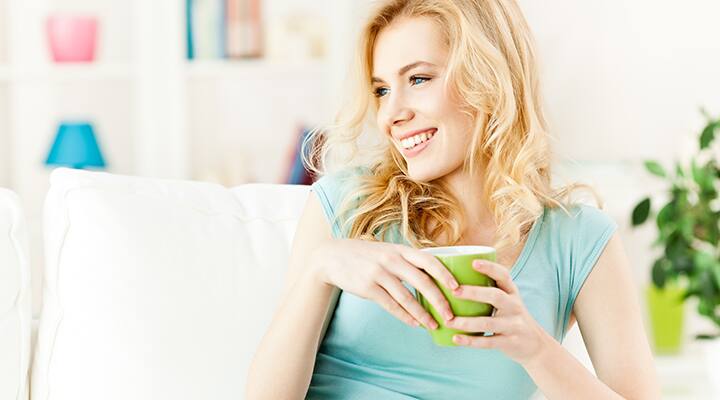 Blond woman drinking green tea on couch