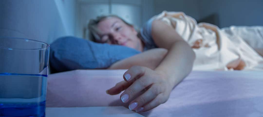 Woman reaching for a glass of water during bedtime