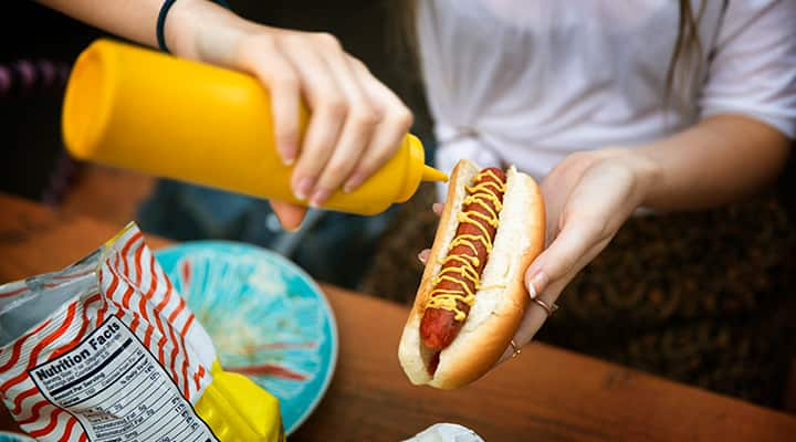 Woman putting mustard onto a hot dog that contain nitrates