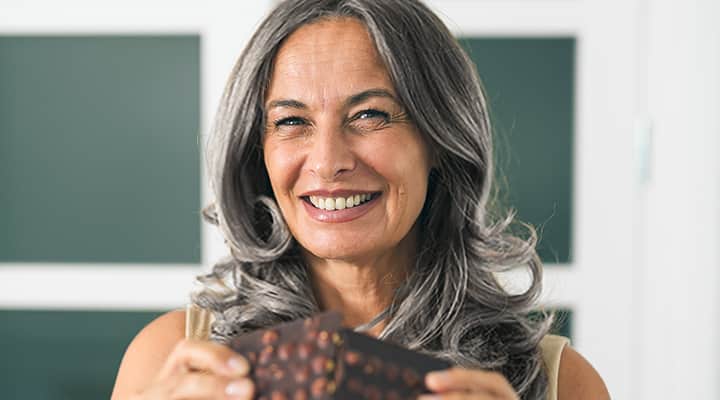 Smiling middle-aged woman breaking a nut-filled chocolate bar