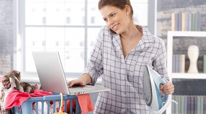 Woman not focused on one task using loptop, cleaning and talking on the phone