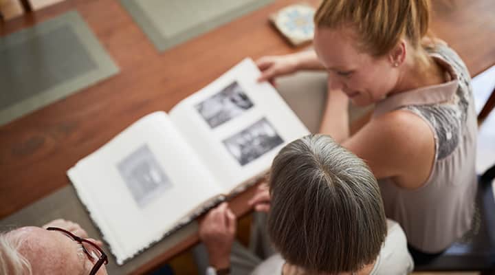 Daughter looking through photo album with senior parents to help with dementia