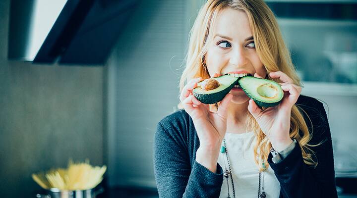 Woman biting into two halves of avocado that fit into different diets