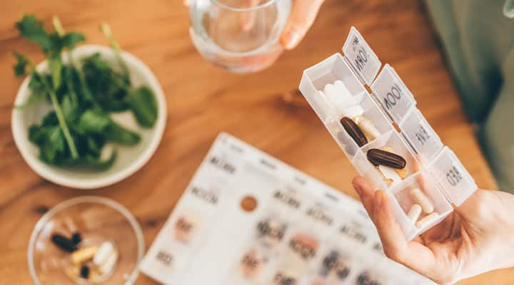 A pill organizer and woman taking supplements.