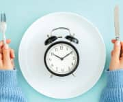 A clock on a plate and a person holding a knife and fork