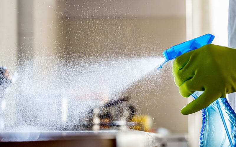 Hand with plastic glove sprying disinfectant over surface