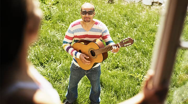 Man playing guitar outside for a woman at her upstairs window